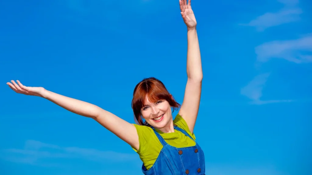 ragazza con i capelli rossi felice ed energica sorride e alza le braccia all'aperto